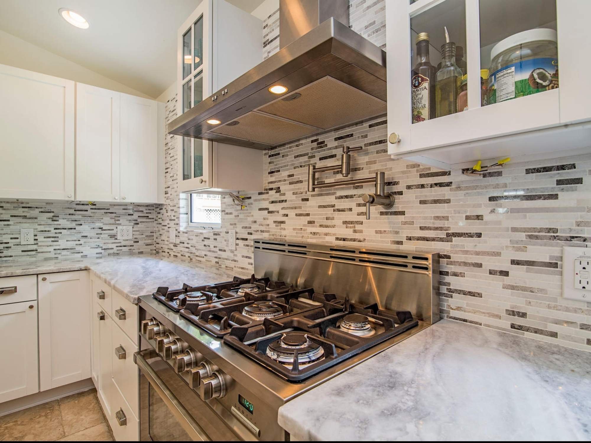 Remodeled kitchen with white cabinetry, stainless steel gas range, pot filler, and mosaic tile backsplash in Southwest F