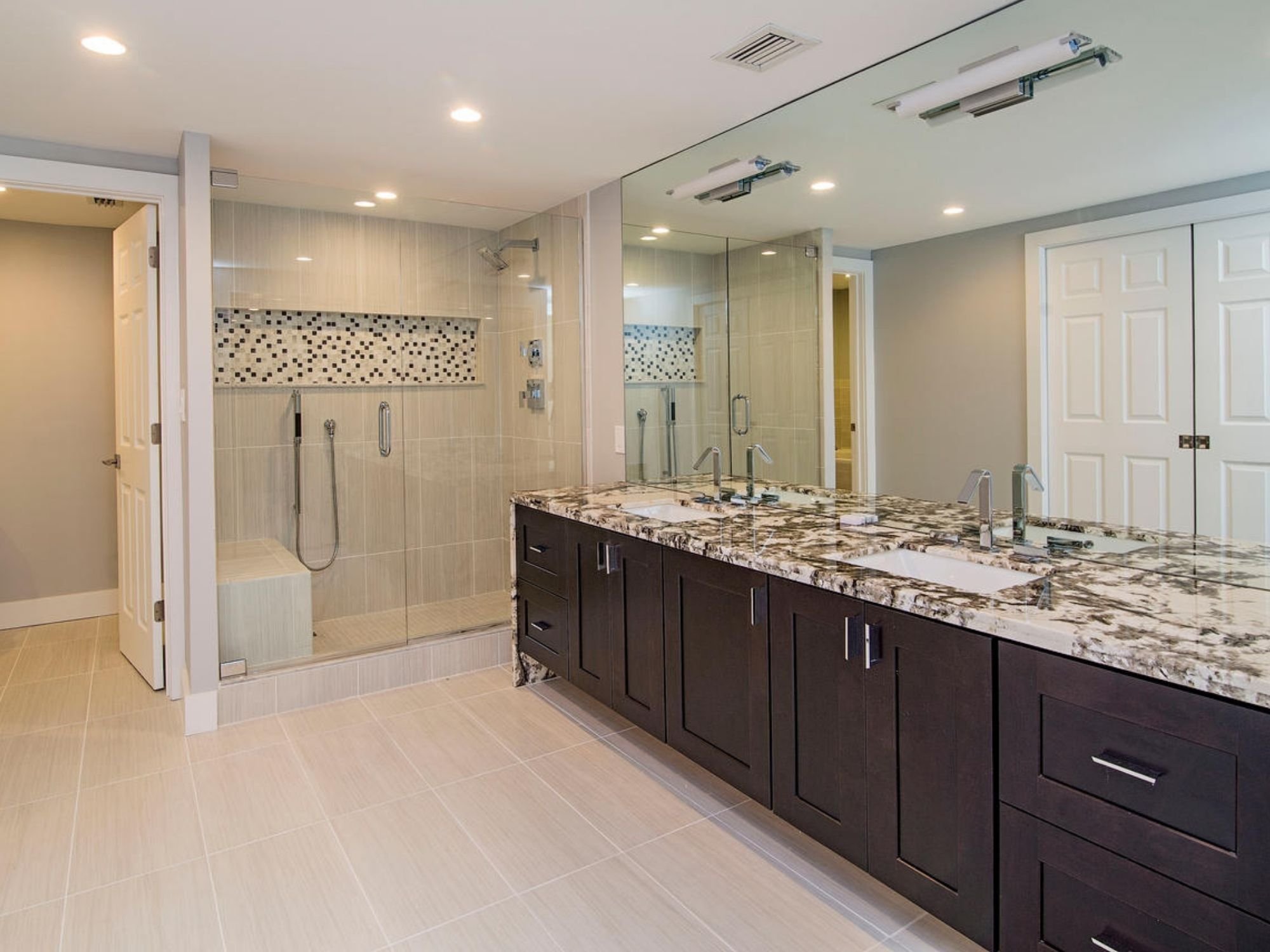 Bathroom with a double vanity, granite countertop, large mirror, and glass-enclosed walk-in shower in Southwest Florida.