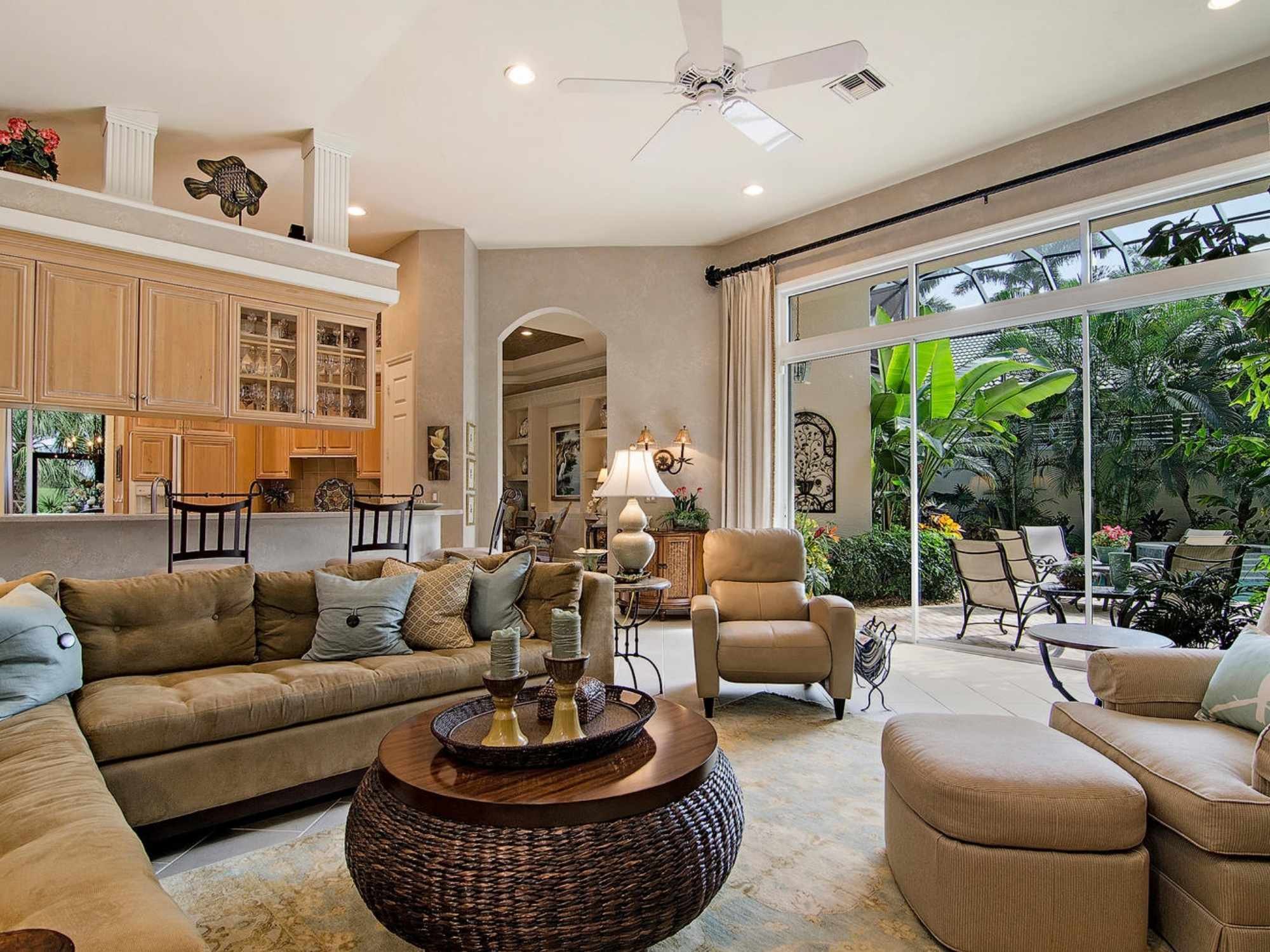Open living room with neutral furnishings, vaulted ceiling, adjoining kitchen, and large patio doors in Southwest Florida.